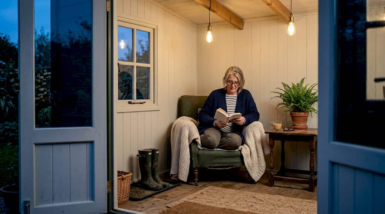 Woman reading in warmly lit garden cabin